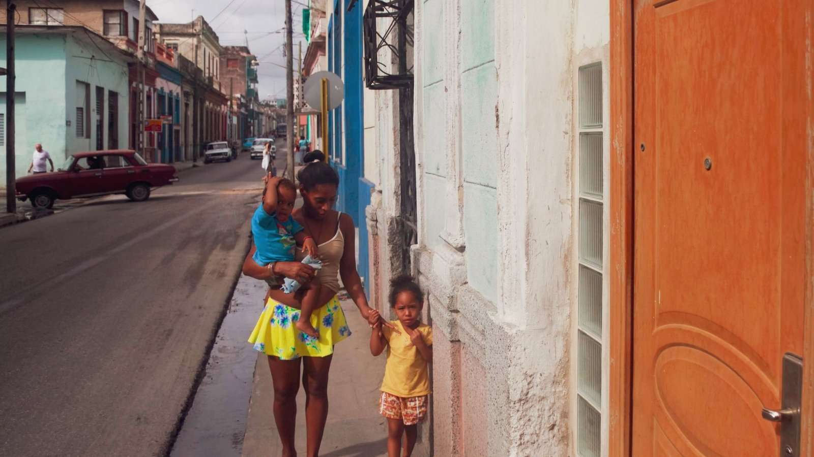 Madre paseando con sus dos hijos por una calle colorida del Caribe